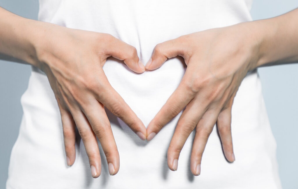 Das Foto zeigt eine Frau die ein Herz aus ihren Fingern formt und vor ihren Bauch hält